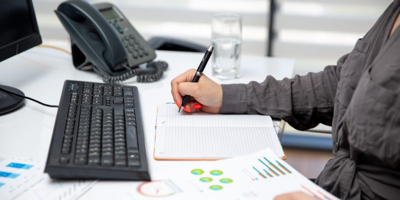 front-view-young-beautiful-businesswoman-working-her-pc-table-along-with-phone-graphics-writing-down-notes-job-activities-technology